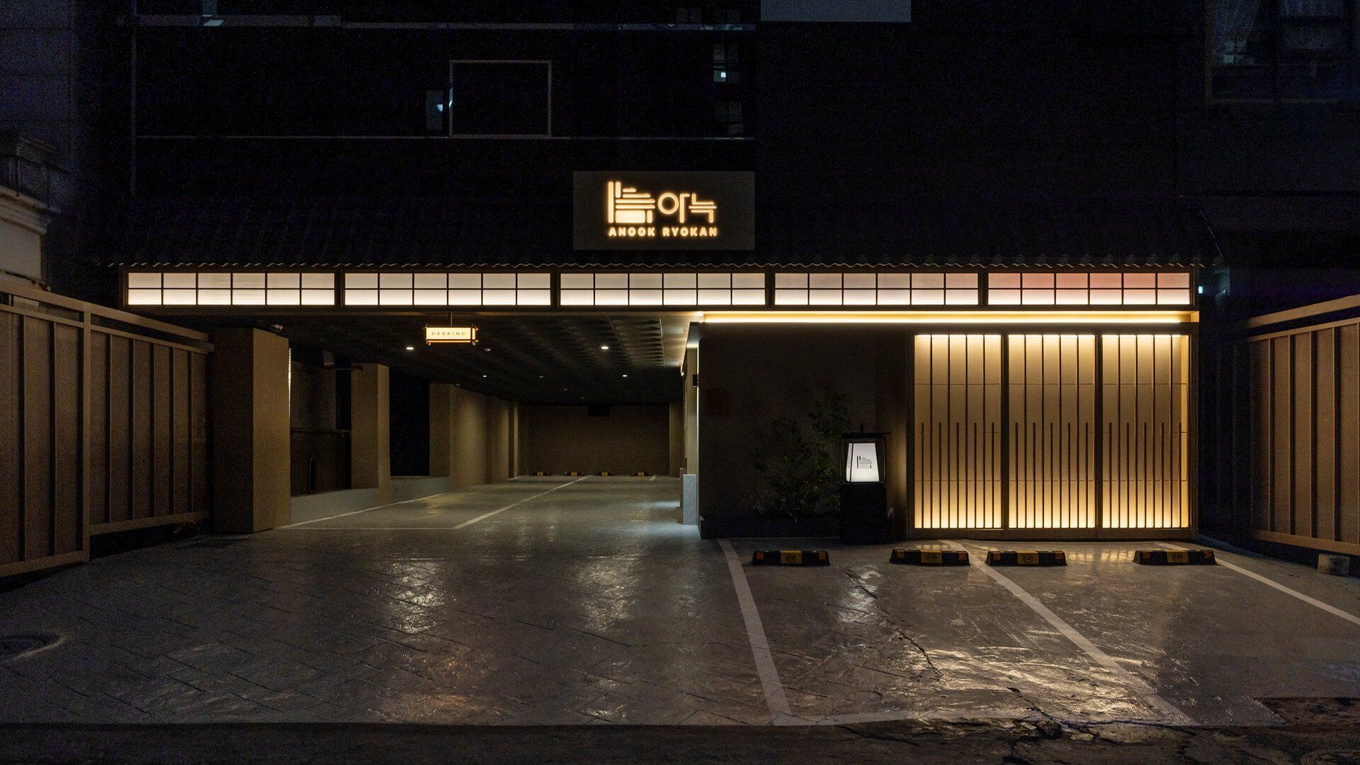 A parking garage entrance with a sign reading 'AnooK Ryokan' and a wooden structure with vertical slats.