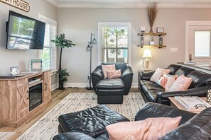 Een woonkamer met een zwarte leren bank, een houten kast, een televisie en een raam met zonwering.