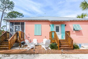 Een roze huis met een houten terras, witte stoelen en een barbecue.