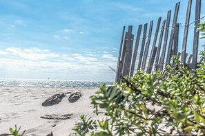 Ein sandiger Strand mit Fußabdrücken, einem Holenzaun und einem klaren Himmel.