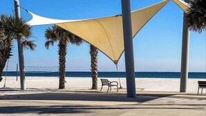 Een wandelpad aan het strand met palmbomen, een bankje en uitzicht op zee.