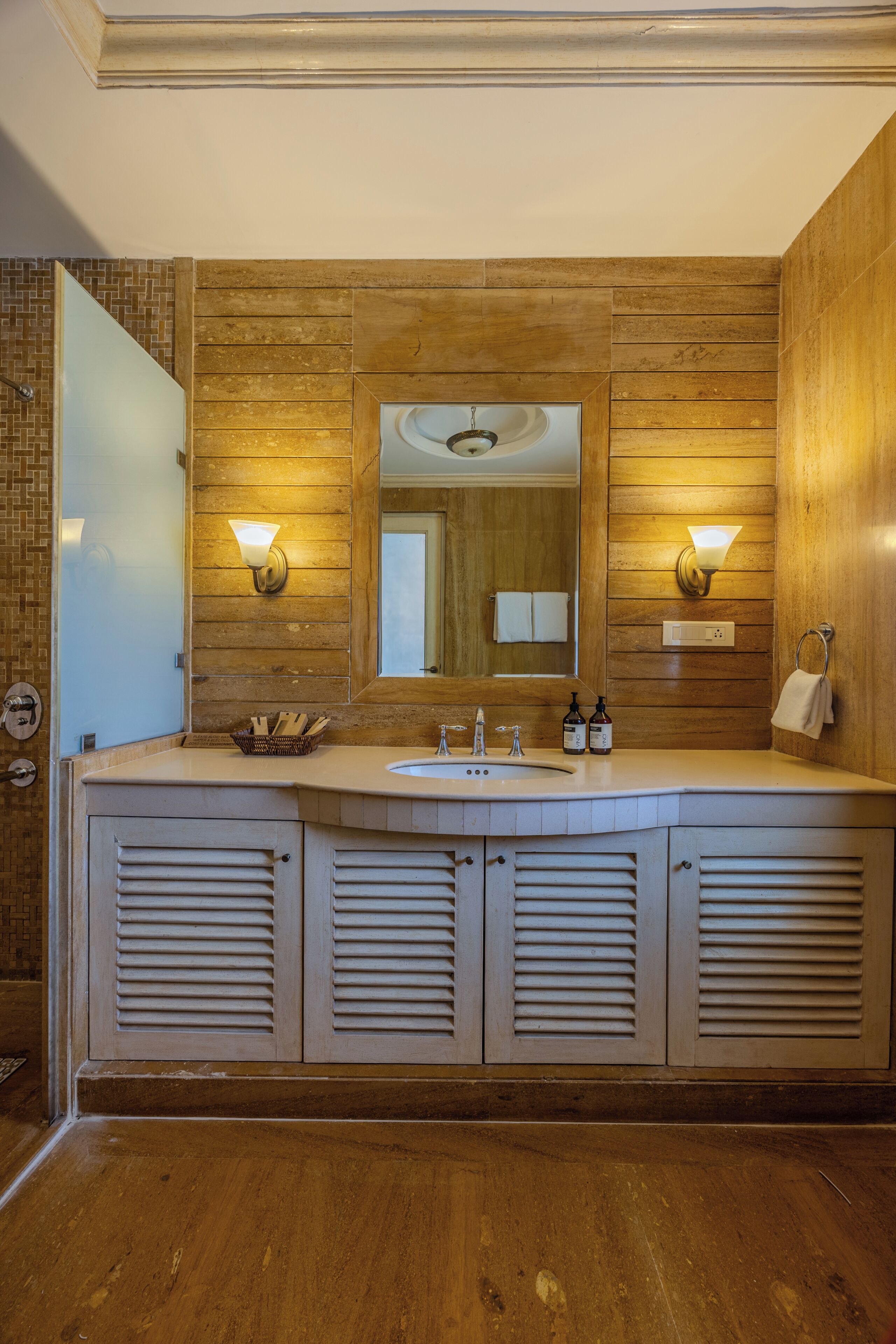 Un baño con paneles de madera, un espejo grande, dos lavamanos e iluminación empotrada.
