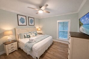 Ein Schlafzimmer mit einem Bett, Nachttischen, einem Deckenventilator, einem Fenster mit Jalousien und einem Kunstwerk an der Wand.