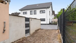 Un immeuble résidentiel avec un toit en tuiles, une entrée fermée par un portail et une allée gravillonnée.