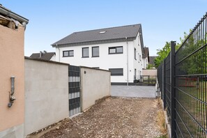 A residential building with a tiled roof, a gated entrance, and a gravel driveway. - Apartment Julia in a New Building with Balcony (Grafschaft)