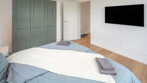 Une chambre à coucher comprenant un lit, une télévision, une armoire et une porte donnant sur une autre pièce.