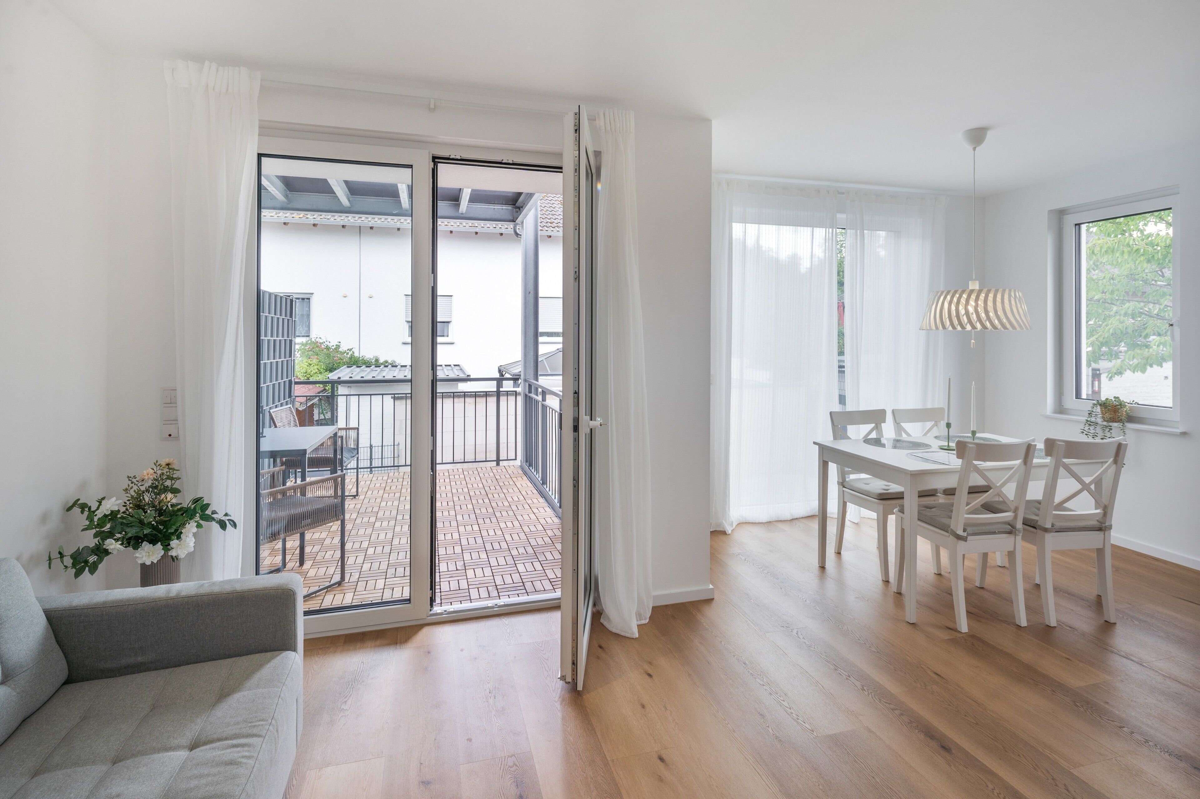 A modern interior with a sliding glass door leading to an outdoor patio, a dining area with a table and chairs, and a grey sofa.