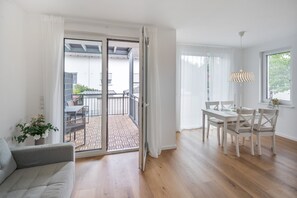 A modern interior with a sliding glass door leading to an outdoor patio, a dining area with a table and chairs, and a grey sofa.