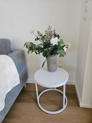 A room with a grey sofa, a white round table with a vase of white flowers, and a wooden floor. - Apartment Julia in a New Building with Balcony (Grafschaft)