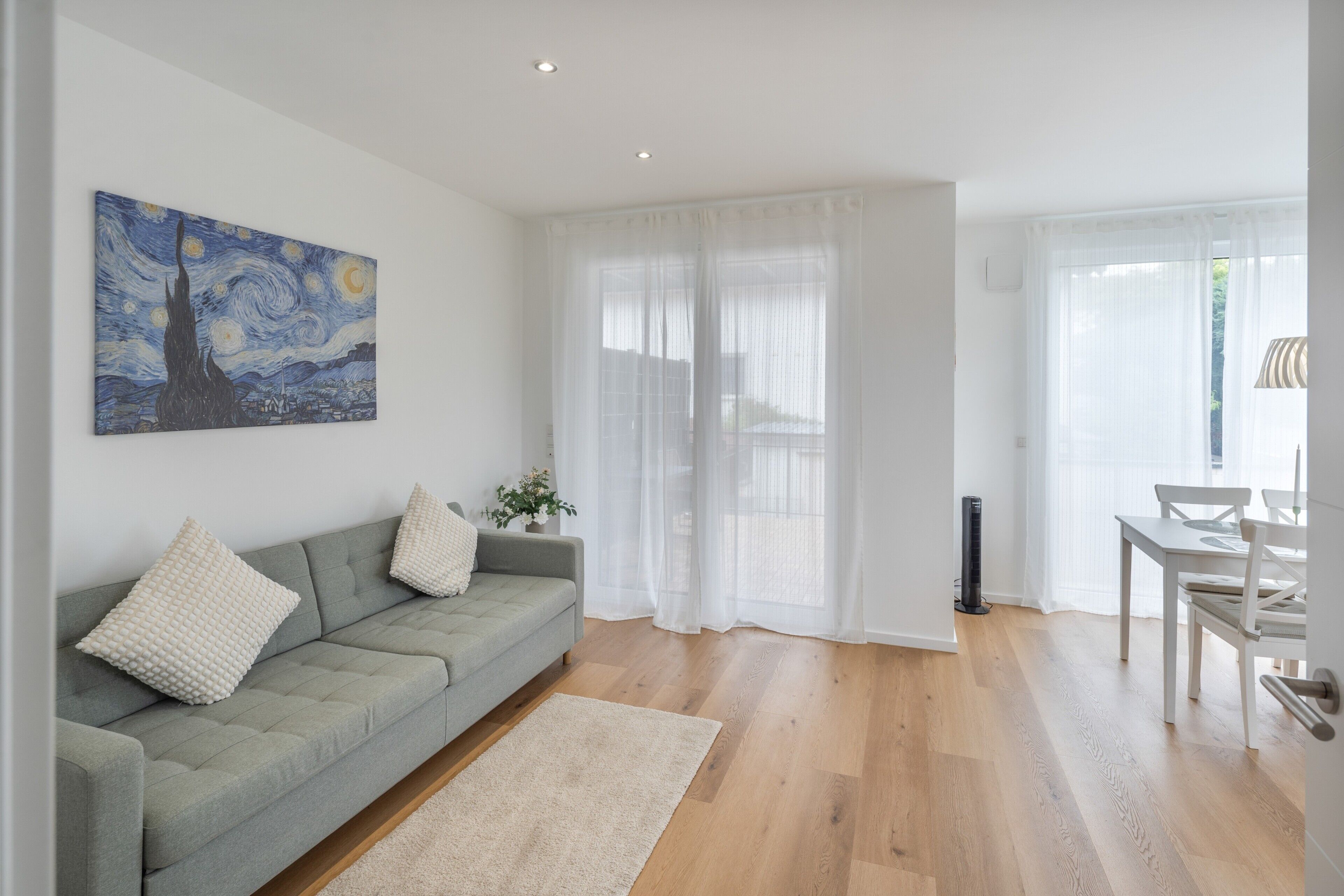 Una sala de estar moderna con un sofá gris, un cuadro y una zona de comedor con mesa y sillas.