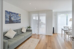 A modern living room with a grey sofa, a painting, and a dining area with a table and chairs.