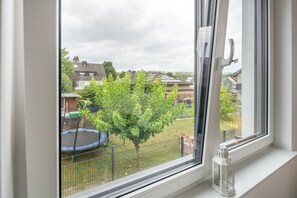 A window with a view of a fenced backyard, a trampoline, and a tree. - Apartment Julia in a New Building with Balcony (Grafschaft)