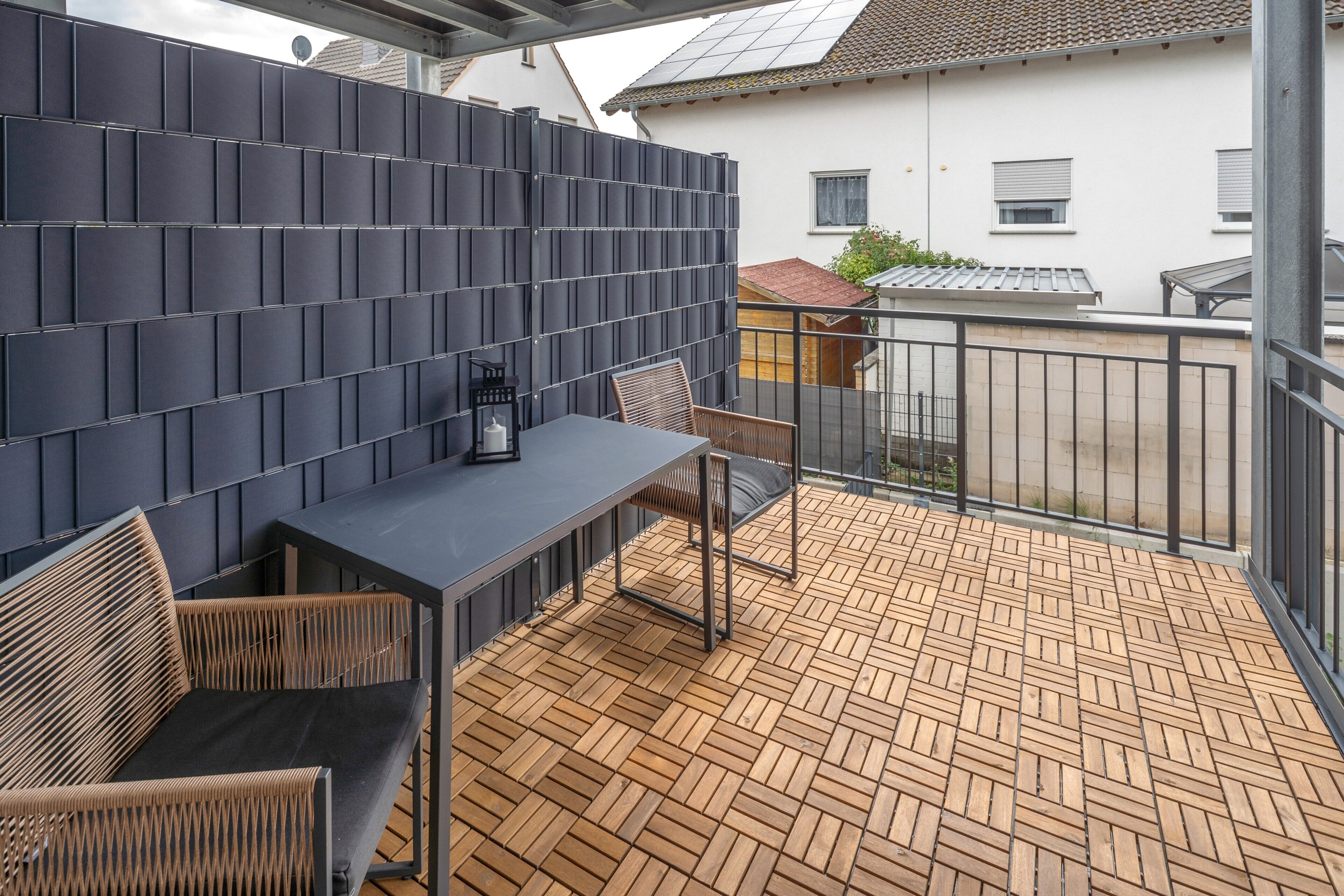 A balcony with a wooden floor, a dark-colored table, and two chairs.