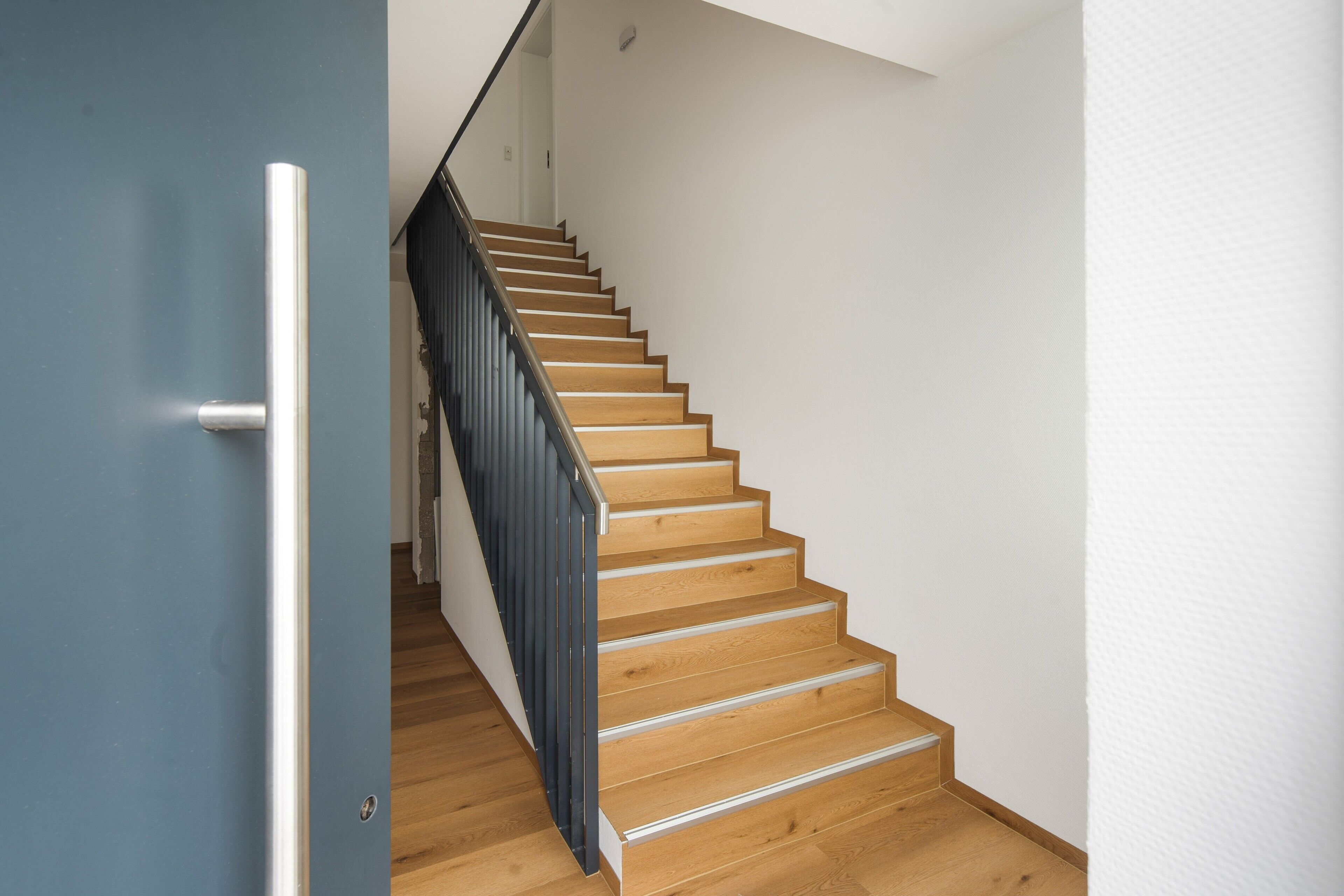 A wooden staircase with a metal handrail and a blue door on the left.