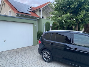 Ein schwarzes Auto parkt vor einem Haus mit rotem Dach, grüner Wand und weißer Garagentür.