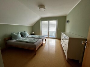 Une chambre à coucher comprenant un lit, une commode, une table de chevet et une fenêtre avec des stores.