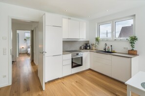 Une cuisine moderne avec des meubles blancs, un four encastré et une fenêtre au-dessus de l’évier.