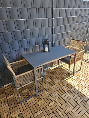 A patio area with a table and two chairs, a lantern, and a wall with a geometric pattern.