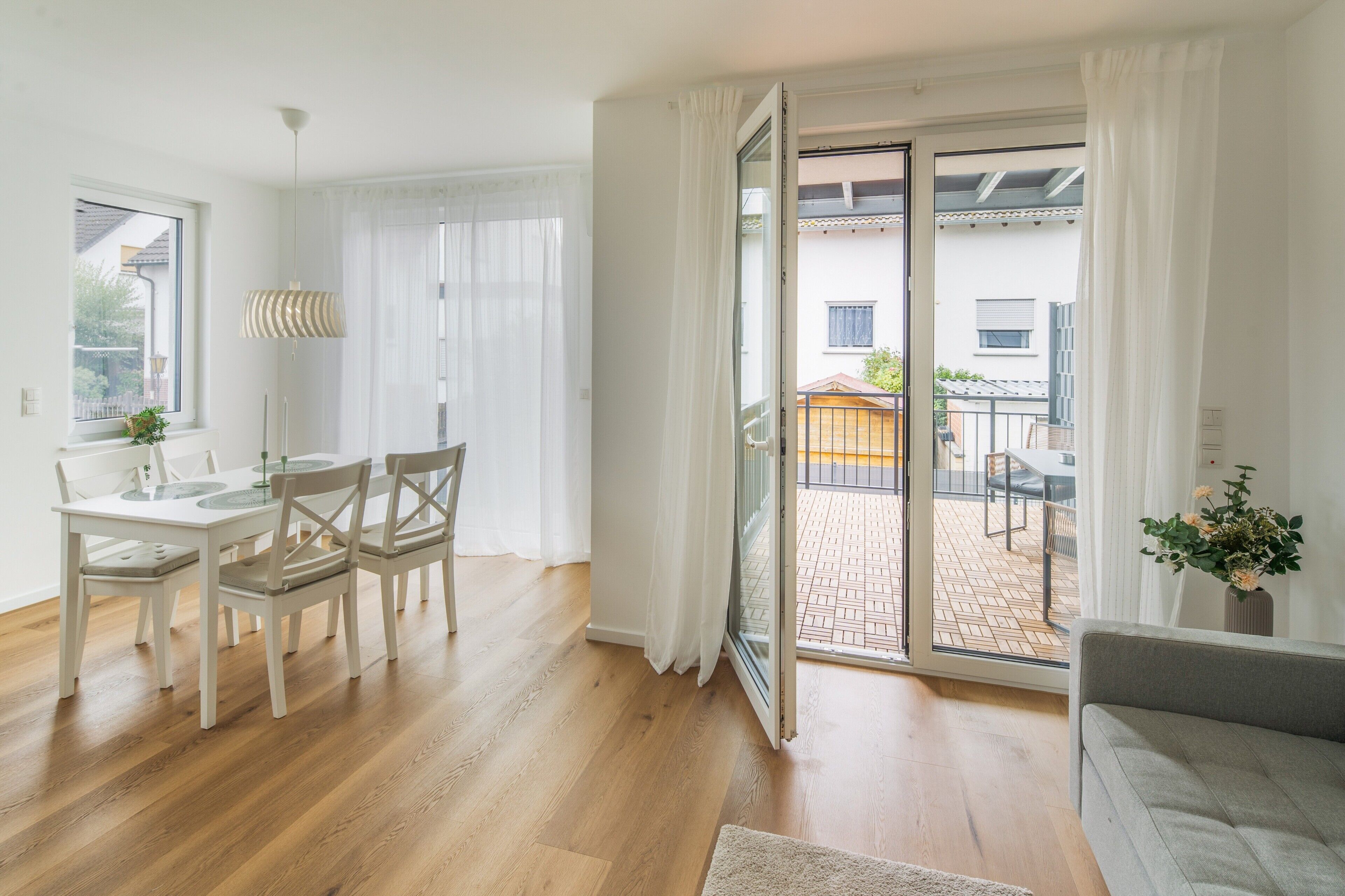 Un salón luminoso con comedor, una puerta corrediza de vidrio que da a un patio exterior y un sofá gris.