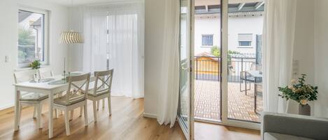 Un salón luminoso con comedor, una puerta corrediza de vidrio que da a un patio exterior y un sofá gris.