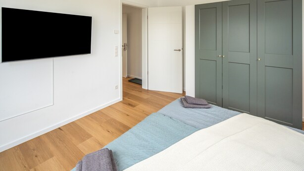 Un dormitorio con una cama, un televisor montado en la pared y un armario.