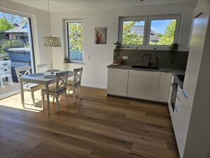 A modern kitchen with a dining area, large windows, and a view of the outside.