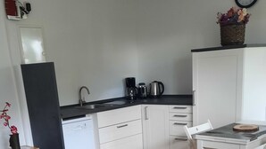 A compact room with a bed, a small table, a chair, a kitchenette, and a clock on the wall. - Vacation Apartment on the Weser River (Elsfleth)