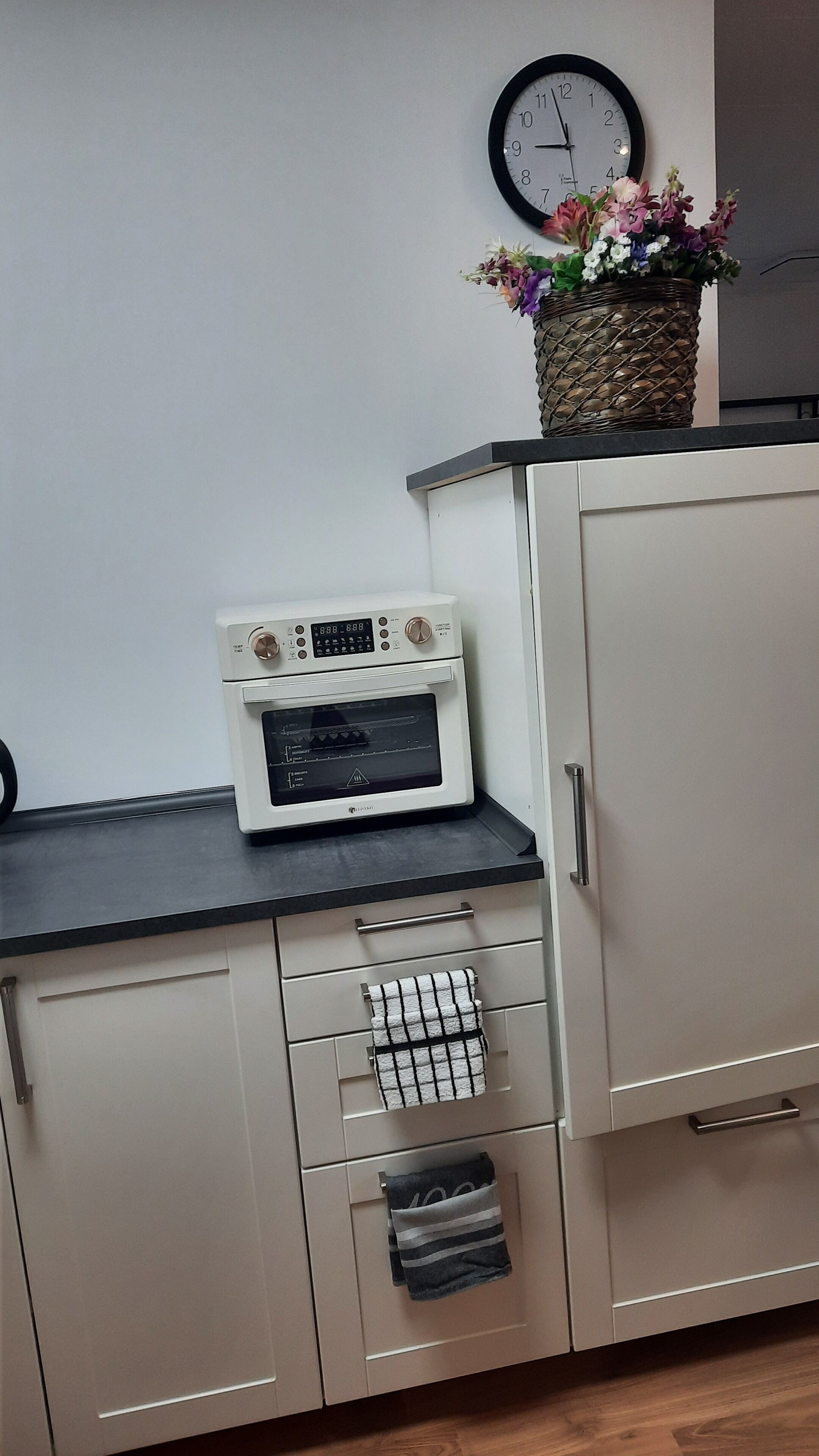 Een kitchenette met een magnetron, oven en een klok aan de muur.