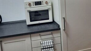A kitchenette with a microwave, oven, and a clock on the wall. - Vacation Apartment on the Weser River (Elsfleth)
