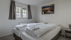 A bedroom with a bed, a window with curtains, a radiator, a nightstand, and a painting on the wall. - Holiday Home in Halfweg With Terrace (Halfweg)