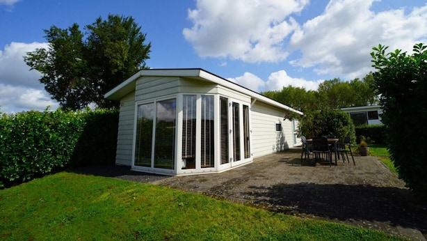 A small, single-story building with large windows and a sloped roof, surrounded by greenery. - Holiday Home in Halfweg With Terrace (Halfweg)