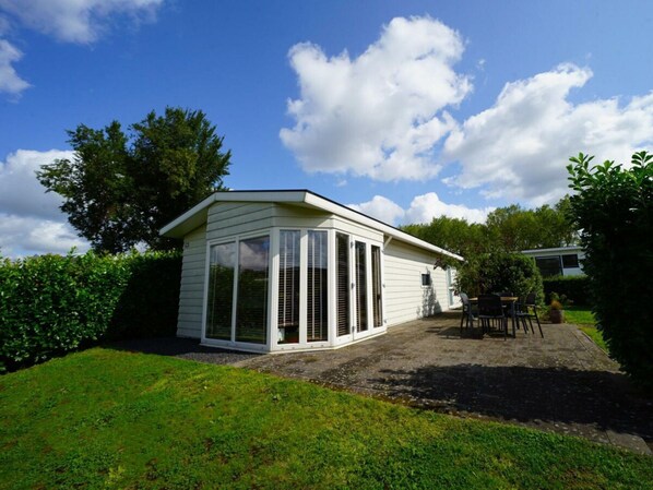 A small, single-story building with large windows and a sloped roof, surrounded by greenery. - Holiday Home in Halfweg With Terrace (Halfweg)