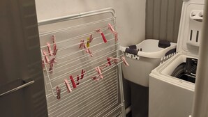 A laundry area with a drying rack, a washing machine, and a window with a view. - Les Hauts de Saint Mamet: On the Road to Spain! (Saint-Mamet)