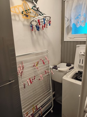 Un espace buanderie équipé d’un étendoir, d’un lave-linge et d’une fenêtre donnant sur un paysage agréable.