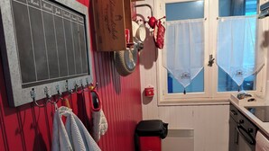 A kitchen with a chalkboard menu, wooden cabinets, a red chair, and a window with curtains. - Les Hauts de Saint Mamet: On the Road to Spain! (Saint-Mamet)