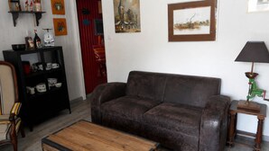A brown sofa, a wooden coffee table, a black side table with a lamp, a red door, and a black shelving unit with various items. - Les Hauts de Saint Mamet: On the Road to Spain! (Saint-Mamet)