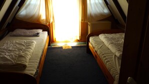 A small, dimly lit room with two beds, a window with curtains, and a radiator. - Föhr Vacation Home 11, 88 sqm with 3 bedrooms (Siegsdorf)