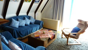 A room with a blue sofa, a wooden armchair, and a small table with a placemat. - Föhr Vacation Home 11, 88 sqm with 3 bedrooms (Siegsdorf)