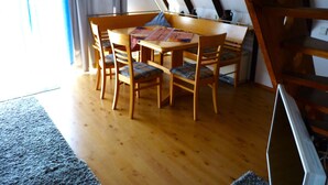 A dining area with a wooden table and chairs, a rug, and a staircase. - Föhr Vacation Home 11, 88 sqm with 3 bedrooms (Siegsdorf)