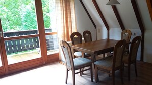 Ein Essbereich mit Holztisch und Stühlen, großen Fenstern mit Vorhängen und Blick auf Grünflächen.