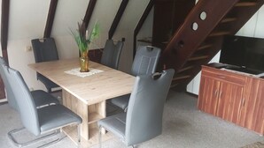 A dining area with a wooden table, four chairs, a vase with plants, and a TV on a wooden cabinet. - Vacation Home at Weidenstraße 3 (Siegsdorf)