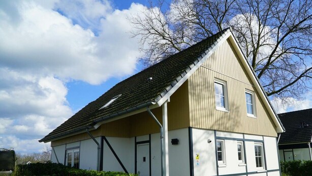 Ein zweistöckiges Haus mit Giebeldach, einer Veranda und einem kleinen Garten mit Blumenbeeten.