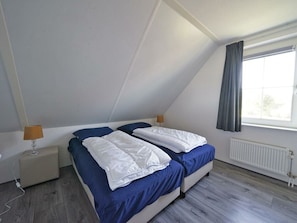 A bedroom with a sloped ceiling, a bed with white bedding, a bedside table with a lamp, and a window with curtains. - Daelenbroeck 12 (Susteren)