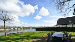 Eine Terrasse mit Tisch und Stühlen, ein Teich und ein Gebäude mit einem Ziegeldach.