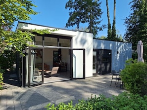 Ein modernes Haus mit Glastür, einer Terrasse und Gartenmöbeln sowie einem kleinen Deck.