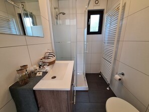 Ein modernes Badezimmer mit einem weißen Waschbecken, einer Dusche und einer Toilette.
