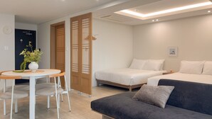Quarto de hotel moderno com uma cama, um sofá, uma mesa de jantar com cadeiras e uma planta decorativa.