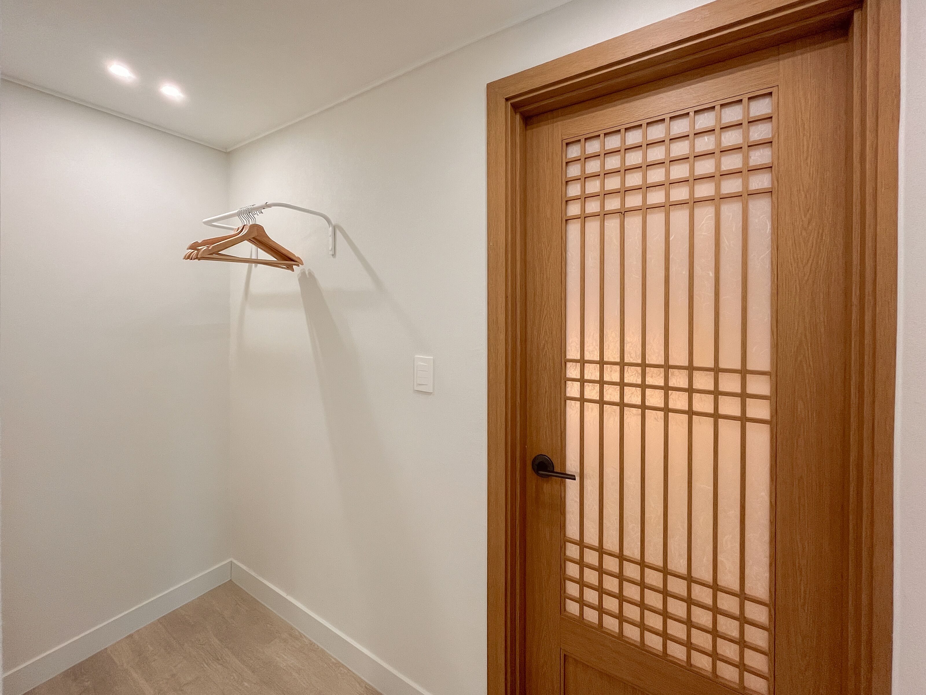 Un pasillo con una puerta de madera con diseño de cuadrícula, una pared blanca y un perchero de madera en la pared.