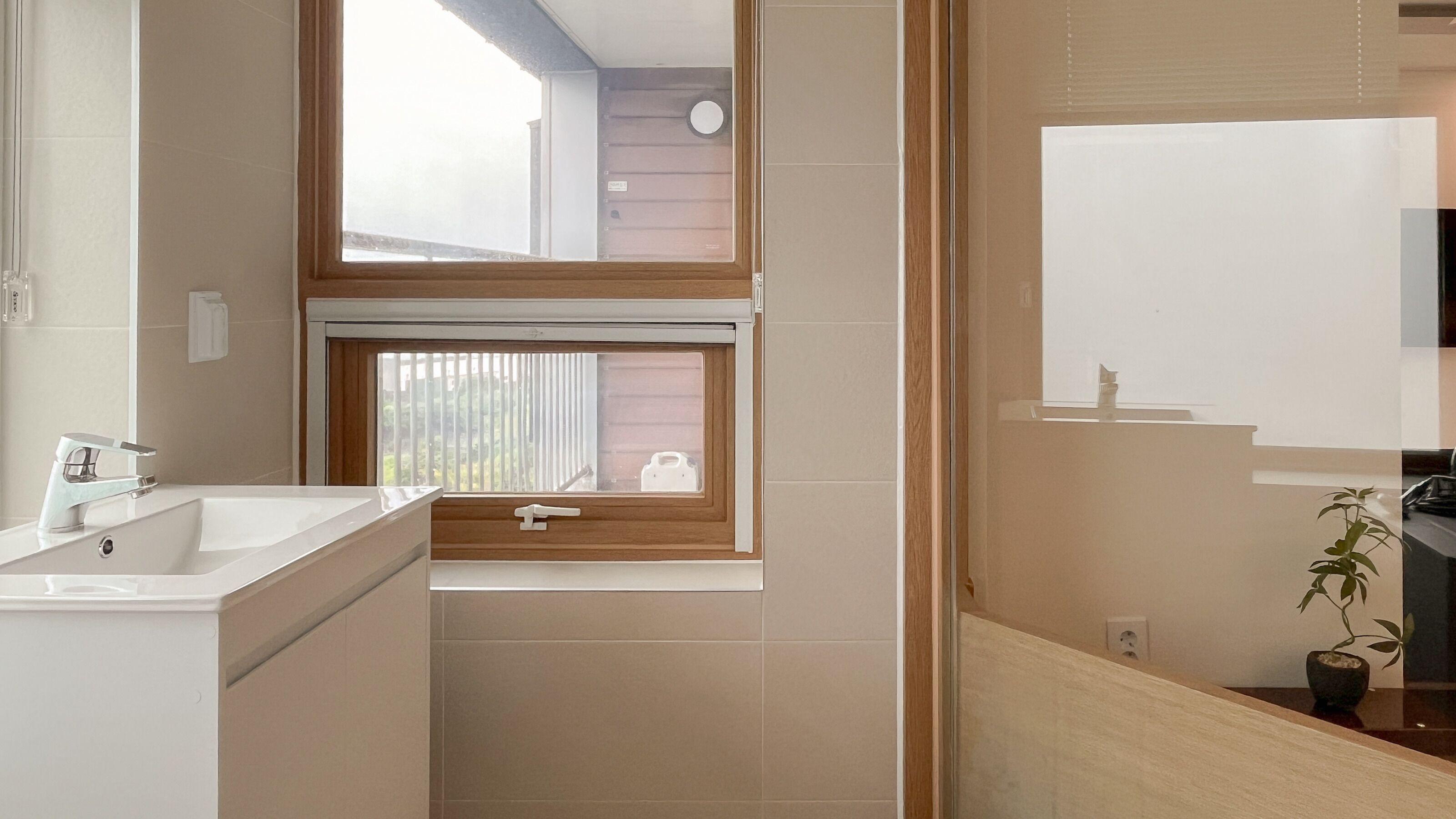Une salle de bain avec un lavabo, un miroir, une fenêtre et une plante en pot.