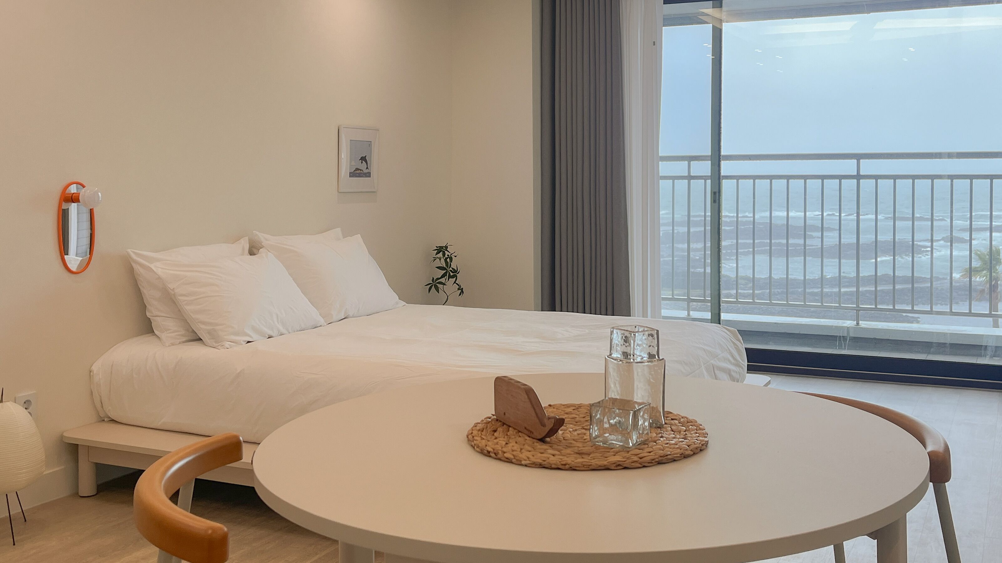 Un dormitorio con cama, una mesa redonda, un espejo y vista al océano.